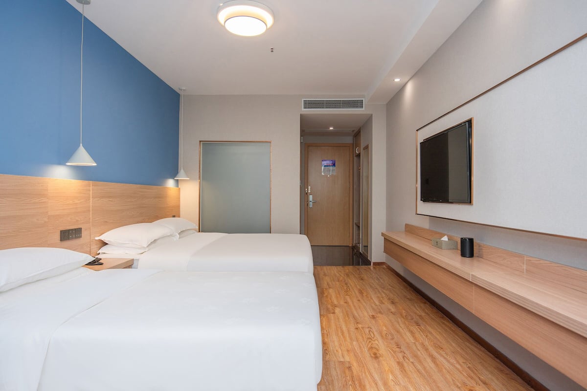 A hotel room with a wooden headboard, a large bed, a flat-screen TV mounted on the wall, and a wooden floor.