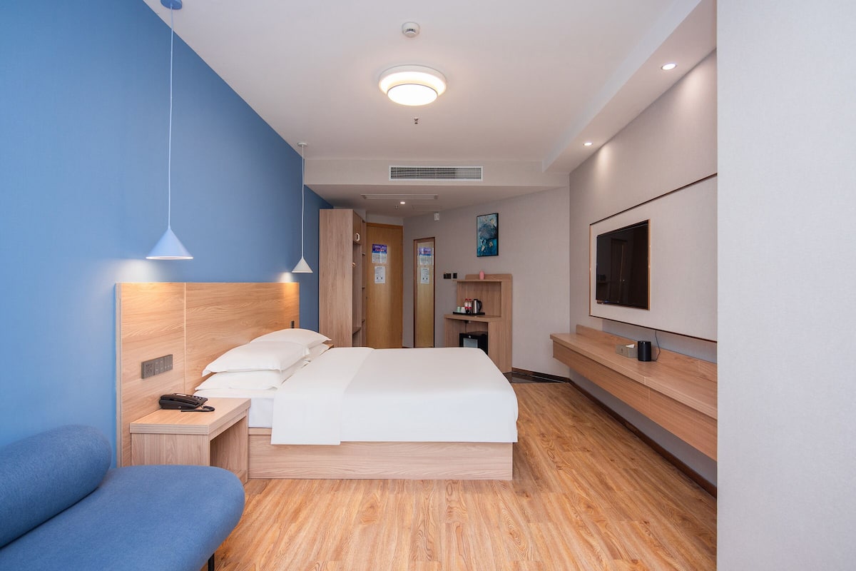 A modern hotel room with a bed, bedside table, and a TV mounted on the wall.