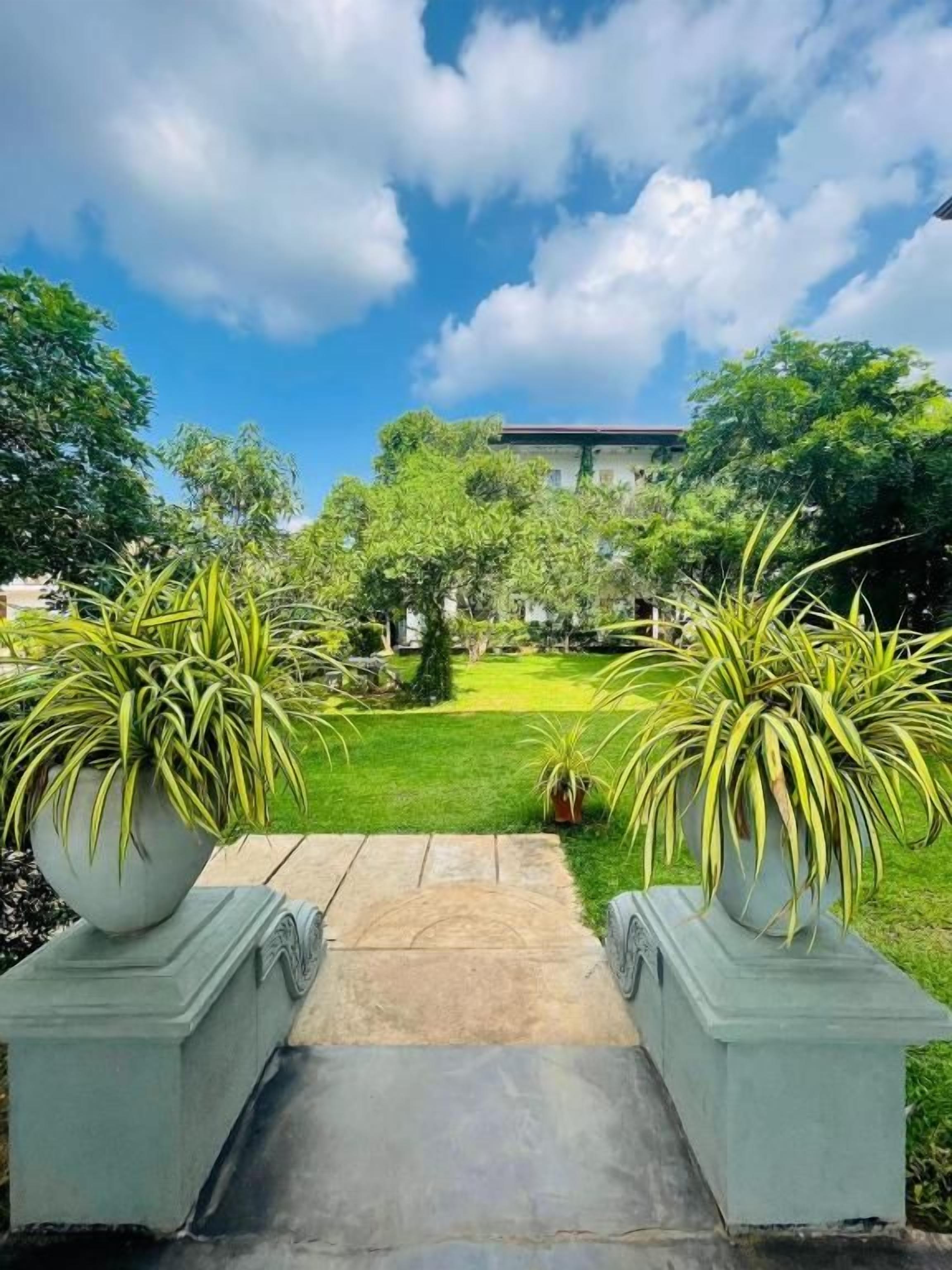A pathway leading to a building with a garden in the foreground and a clear sky above.