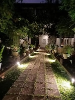 Un sendero pavimentado flanqueado por macetas con plantas, que conduce a un edificio con una puerta.