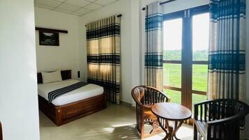 A hotel room with a bed, a table, and chairs, a window with curtains, and an air conditioning unit.