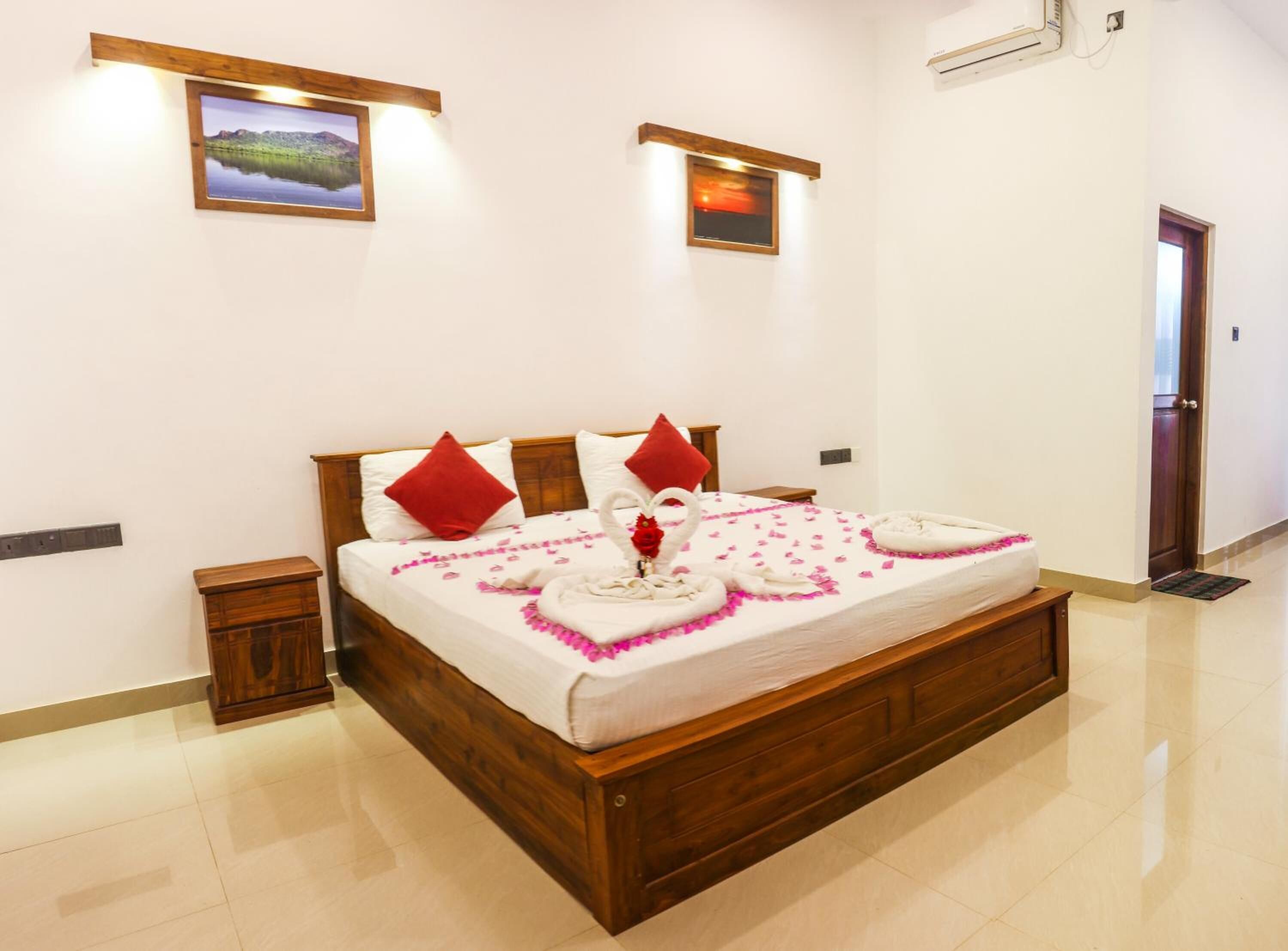 Habitación de hotel con una cama de madera, dos almohadas rojas, un ramillete de flores y una decoración con forma de corazón sobre la cama.