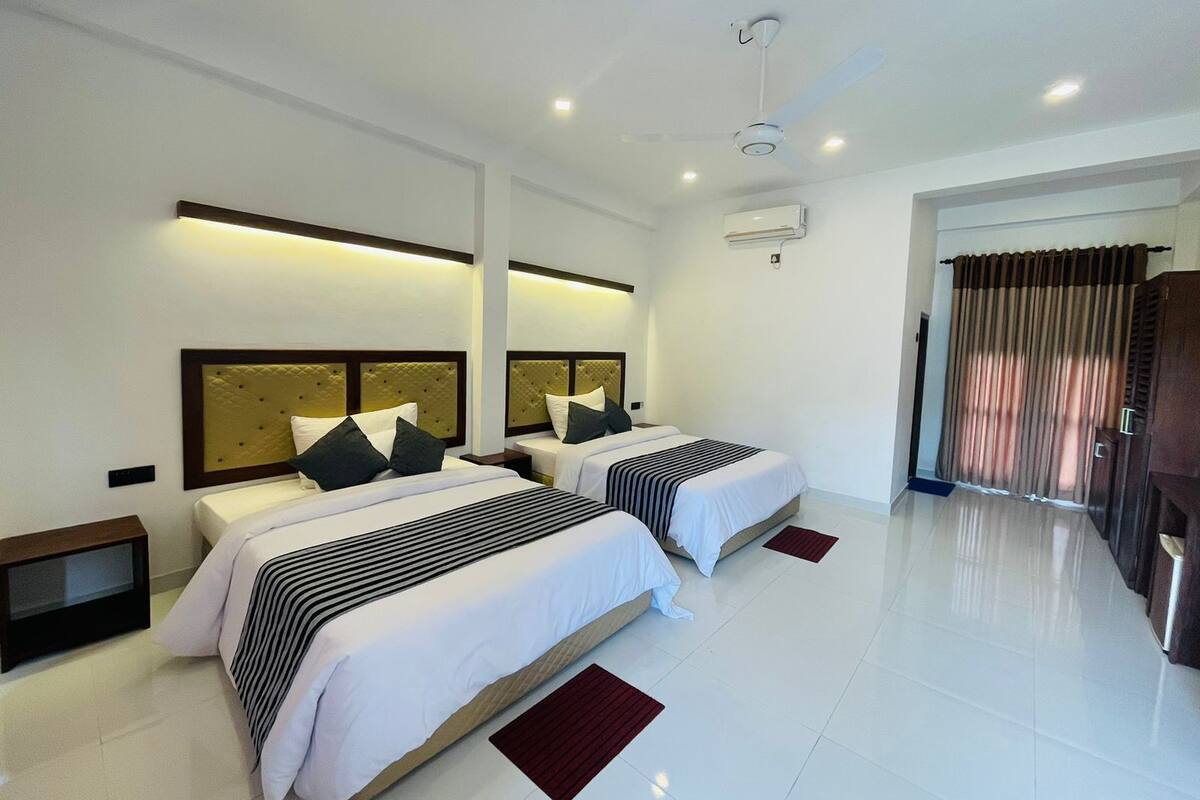 Een moderne hotelkamer met twee bedden, een plafondventilator en een groot raam met gordijnen.
