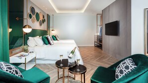 A modern hotel room with a large bed, two green armchairs, a small table with two glasses of champagne, a bedside table with a lamp, and a flat-screen TV mounted on the wall. - La Seine Boutique Hotel (Vientiane)