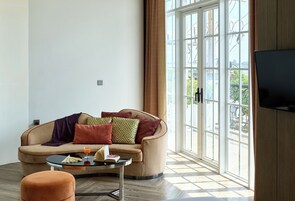 Sala de estar con sofá, mesa de centro y reposapiés, con ventanas amplias y televisor.