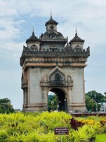 A large, ornate gateway with intricate carvings and multiple spires, surrounded by lush greenery and a sign instructing not to step on the grass.