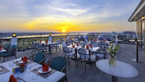 An outdoor dining area with tables and chairs, overlooking a sunset over a body of water. - La Seine Boutique Hotel (Vientiane)