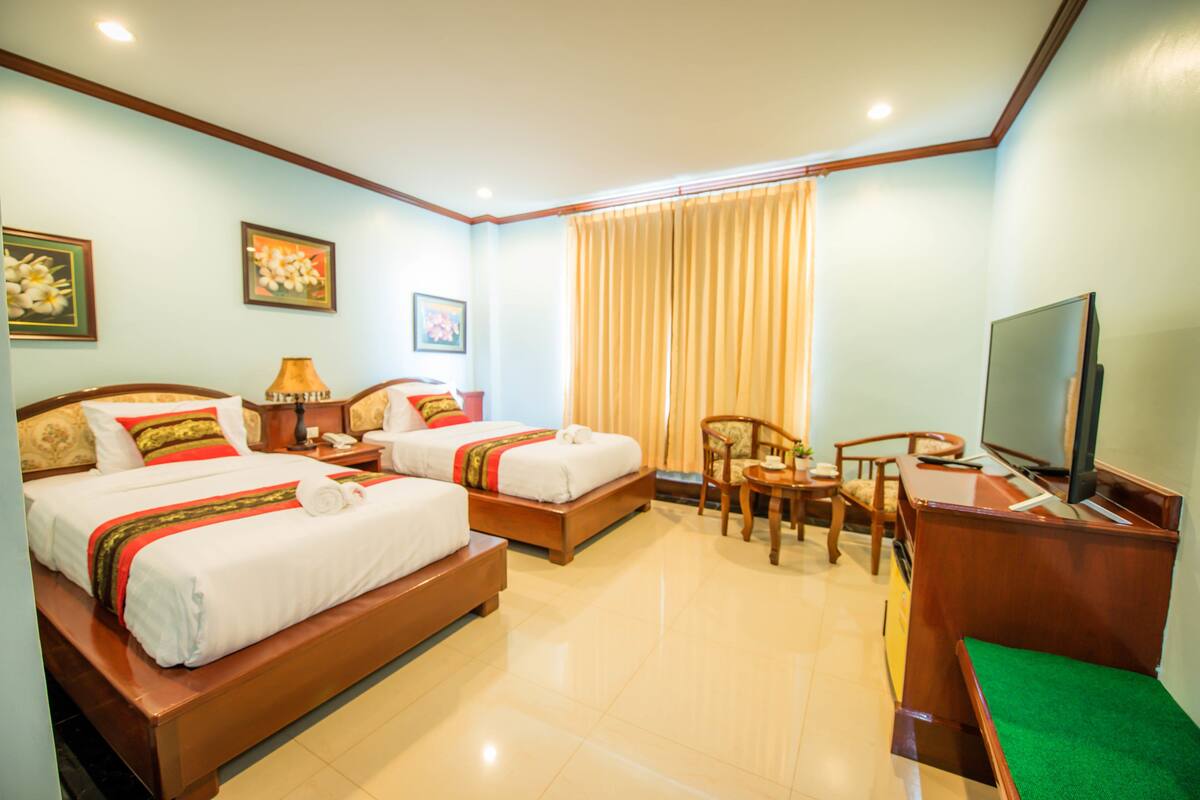 A hotel room with two beds, a desk, a chair, a television, and a window with curtains.