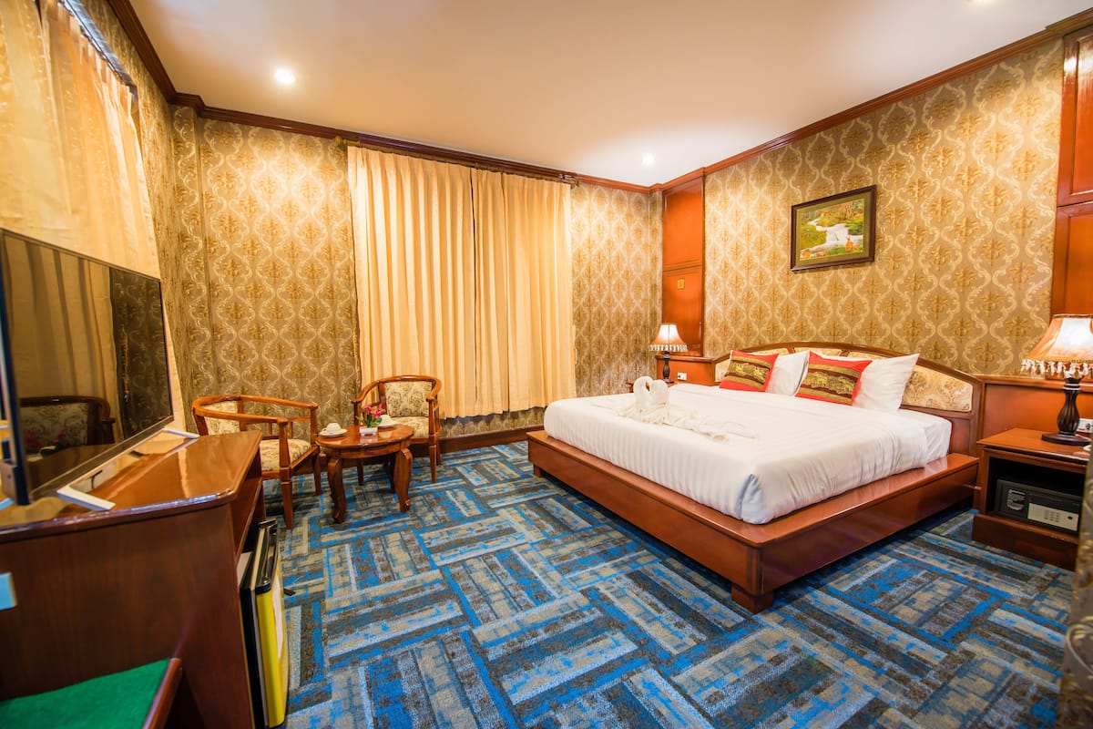 A hotel room with a large bed, a desk, a chair, a small table, and a TV.