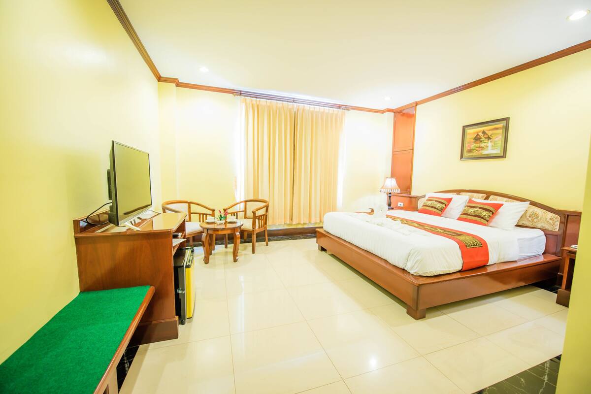 A hotel room with a bed, desk, chairs, and a television.