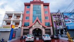 A multi-story building with a prominent entrance, several parked cars, and a wet street. - Soubandith Hotel (Pakse)