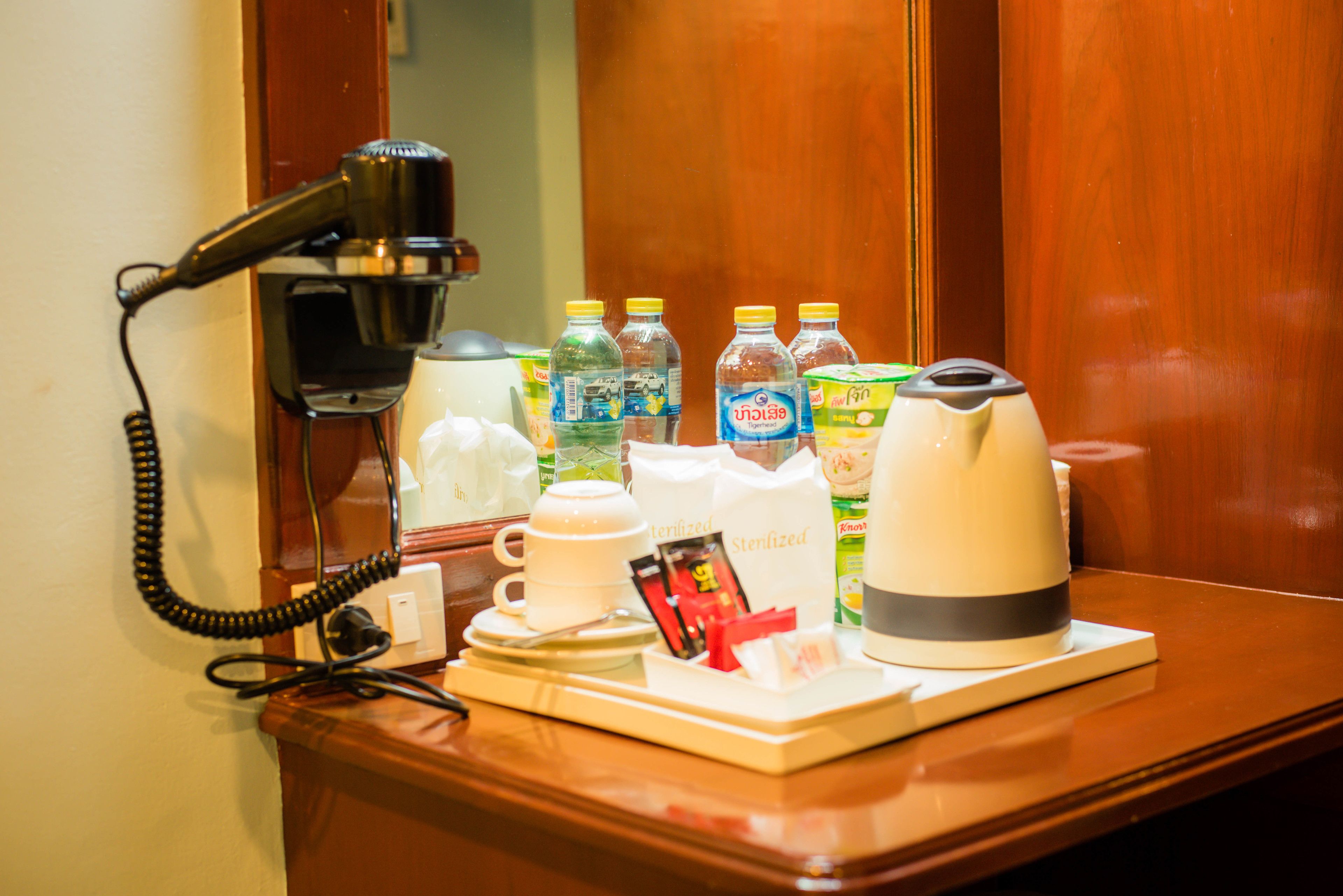 Un bureau dans une chambre d’hôtel, équipé d’un sèche-cheveux, d’une machine à café et de diverses boissons en bouteille.