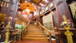 A grand wooden staircase with ornate railings and a chandelier, leading to a higher floor. - Soubandith Hotel (Pakse)
