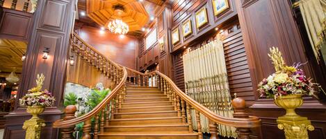 Una imponente escalera de madera con barandillas ornamentales y un candelabro, que conduce a un piso superior.