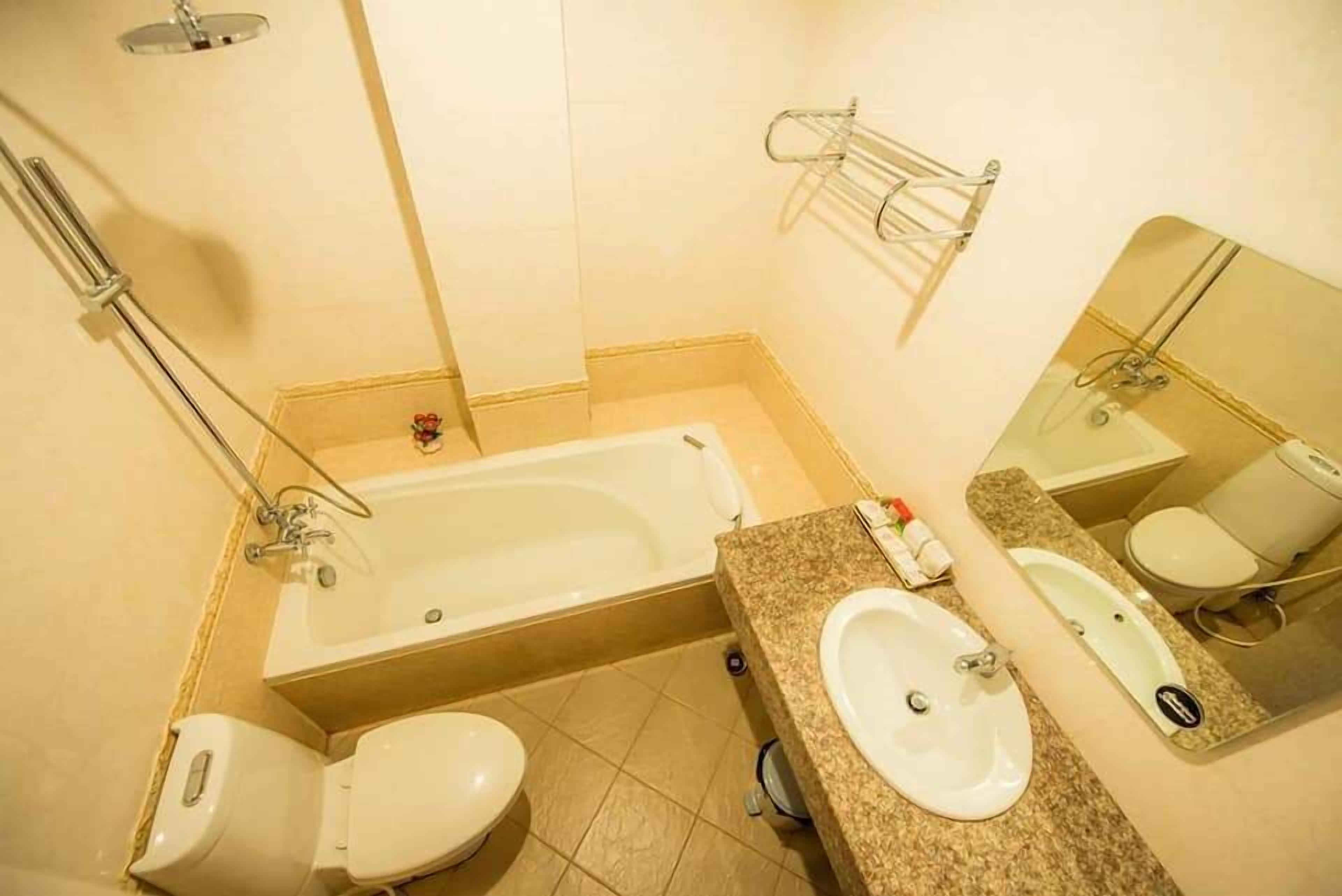 A bathroom with a bathtub, two toilets, a sink, and a mirror.