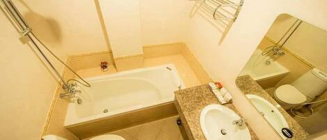 A bathroom with a bathtub, two toilets, a sink, and a mirror.