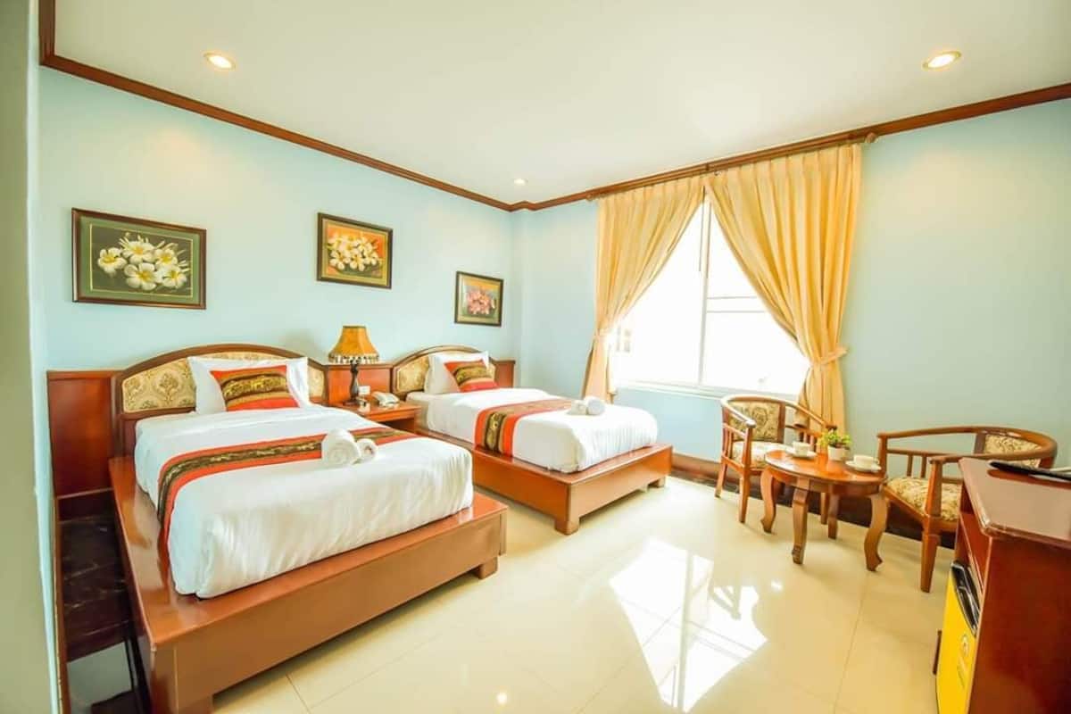 A hotel room with two beds, a desk, a chair, and a window with curtains.