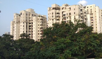 A multi-story residential building with balconies and a dense tree in the foreground.