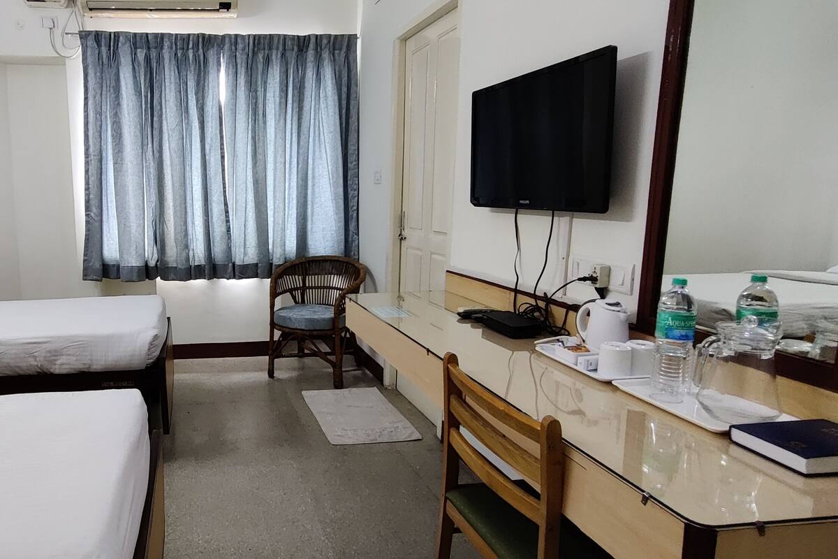 Een hotelkamer met twee bedden, een bureau, een stoel, een televisie en een raam met gordijnen.