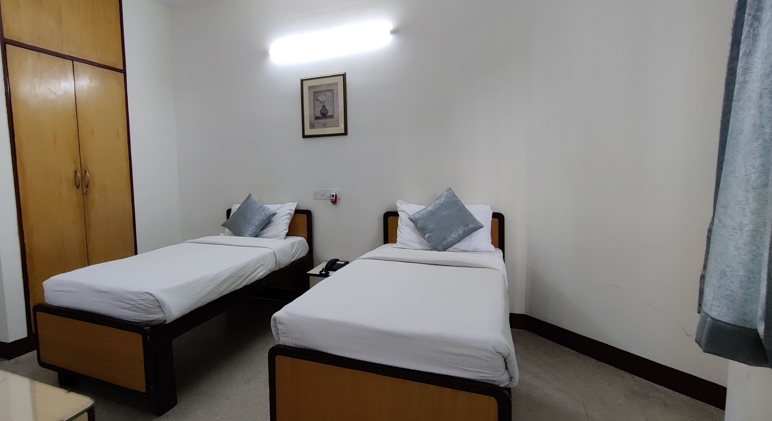 A room with two single beds, a wooden wardrobe, a framed picture on the wall, and a telephone on the nightstand.
