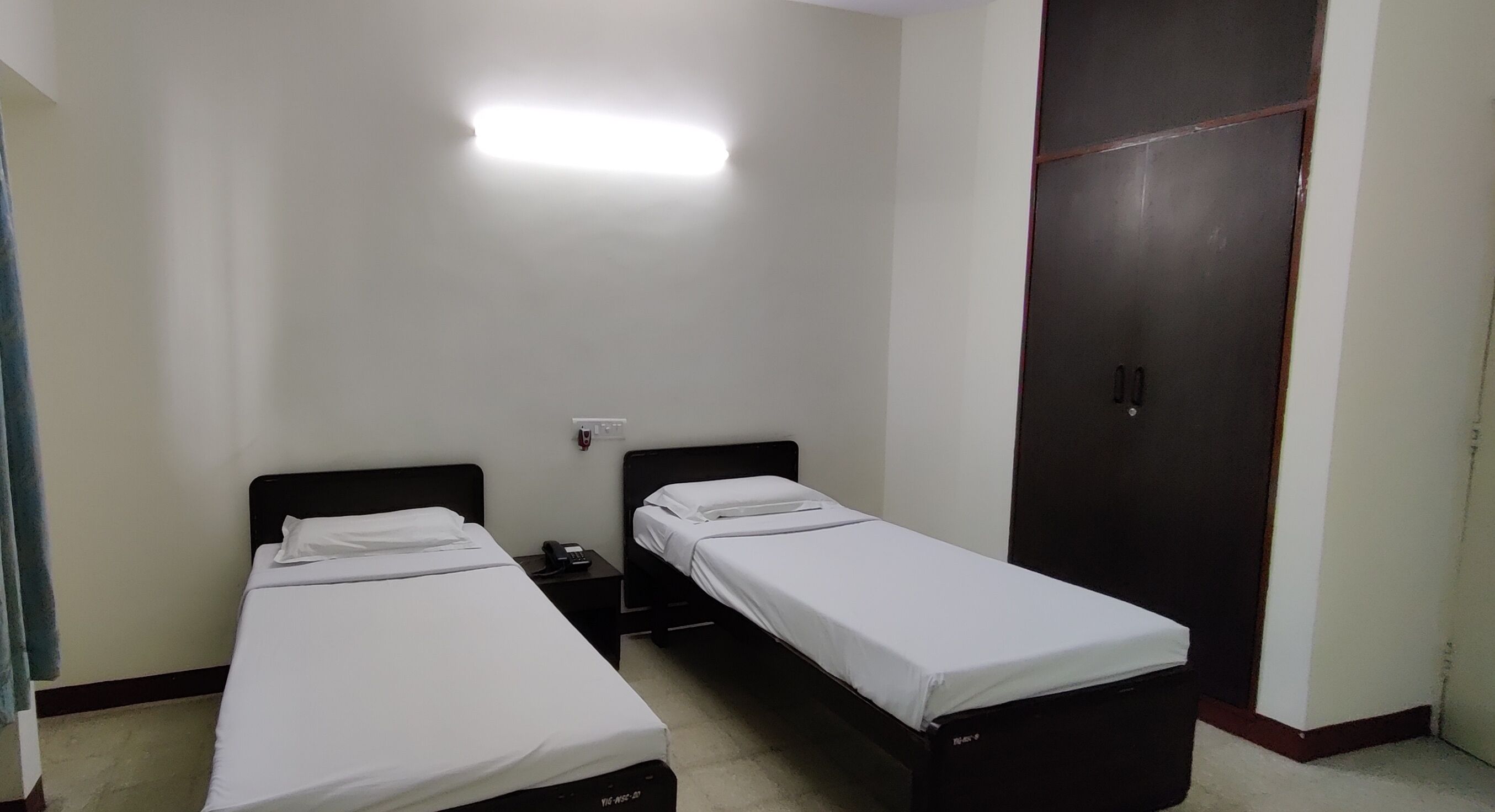 A room with two single beds, a wardrobe, and a bedside table with a phone.