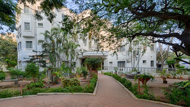 A pathway leading to a building labeled "International Guest House" with a garden and potted plants in front.