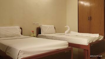Two single beds with wooden frames and white bedding, a wooden wardrobe, and a small table with a red flower.