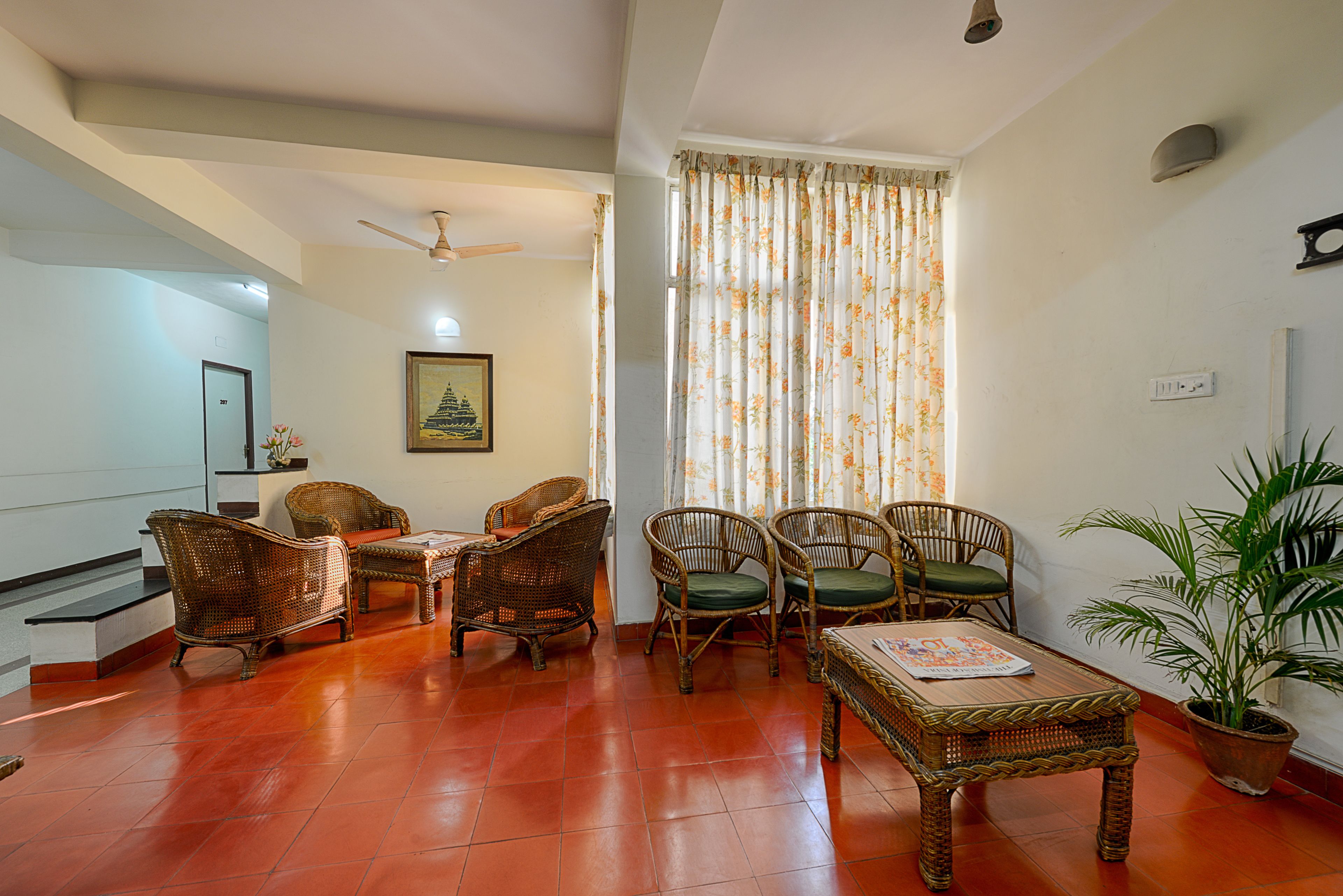 A living room with wicker furniture, a ceiling fan, a potted plant, and a window with floral curtains.