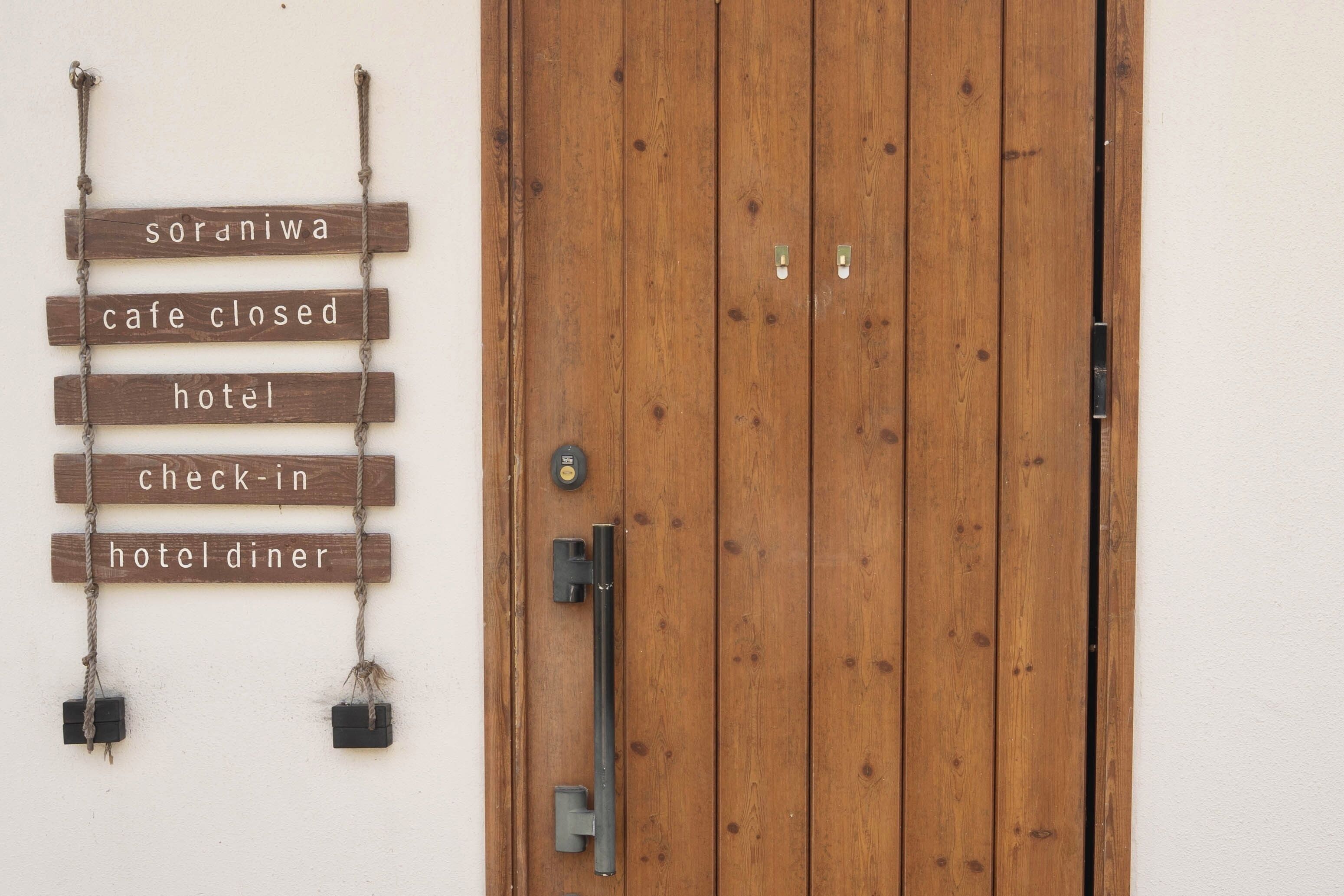 A wooden door with a sign indicating 'soraniwa cafe closed hotel check-in hotel diner' and a metal handle.