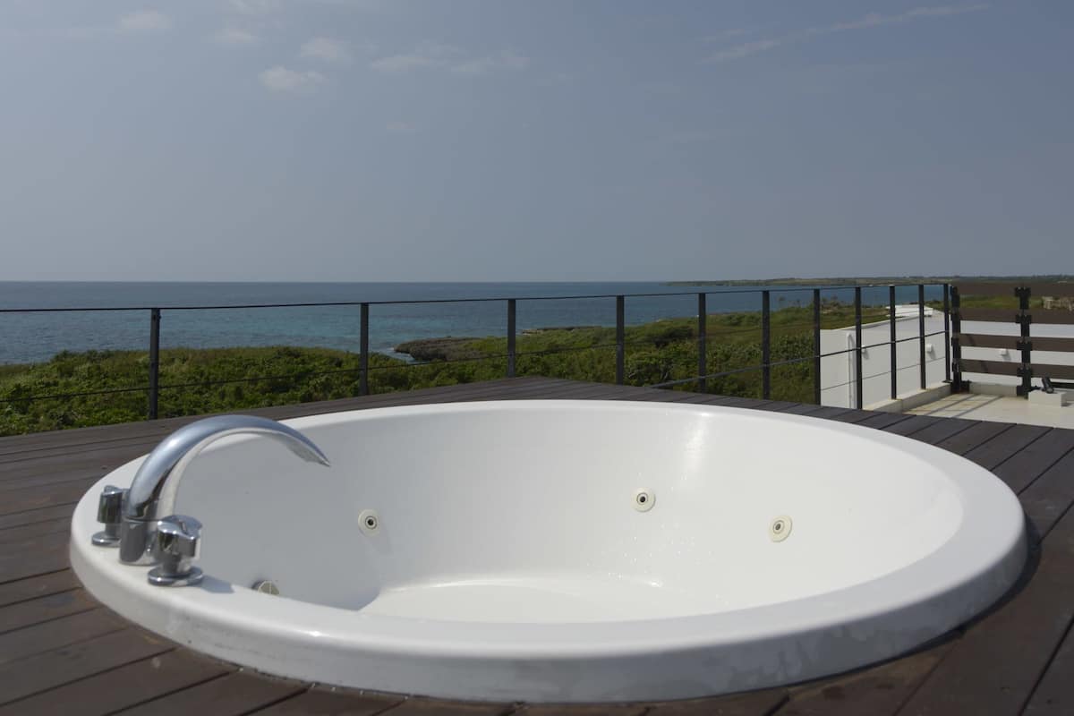 A white hot tub on a wooden deck with a view of the ocean.