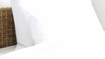 A bed with white linens and a brown woven pillow.