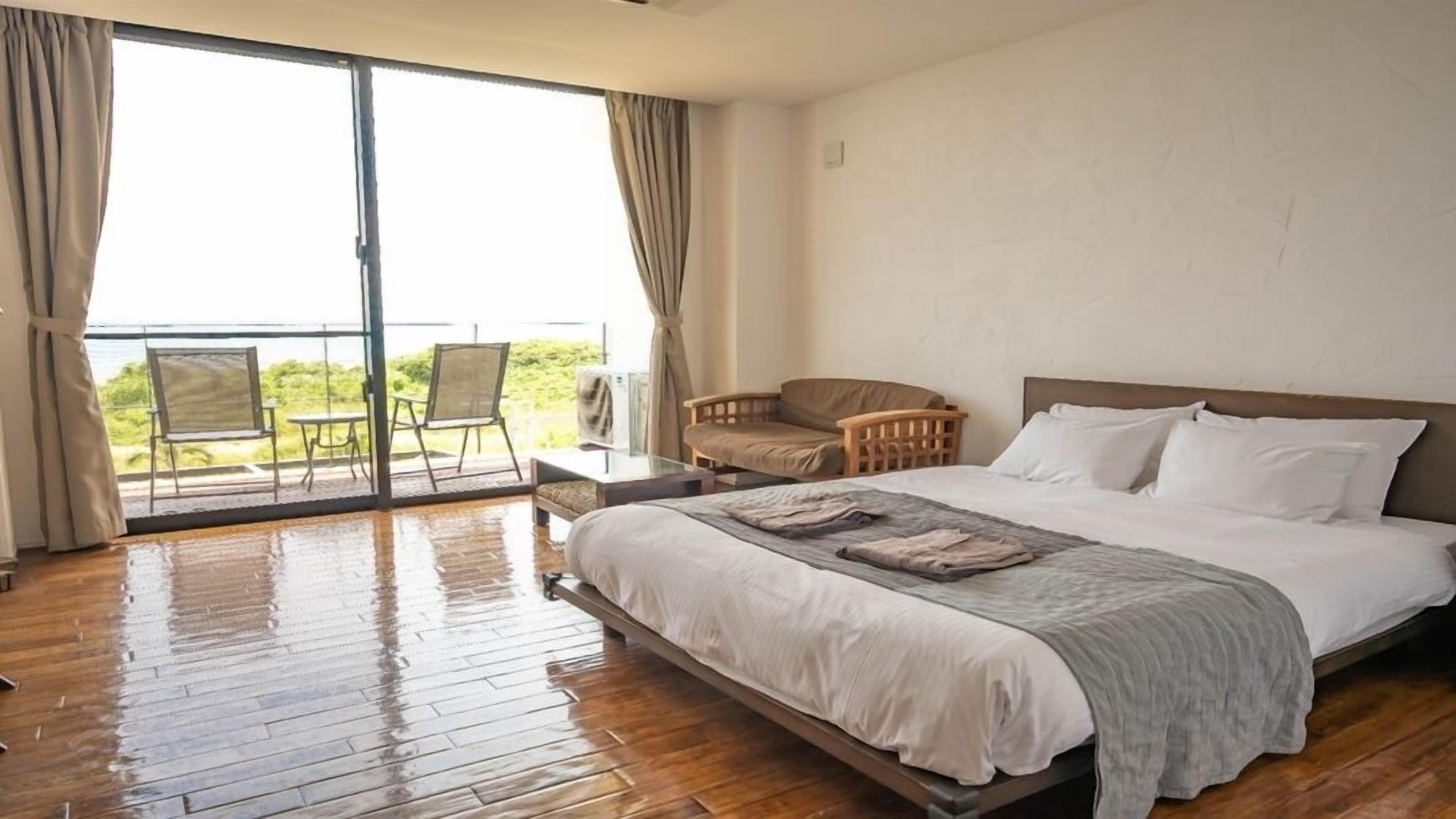 A bedroom with a large bed, a sofa, a chair, and a balcony with a view.