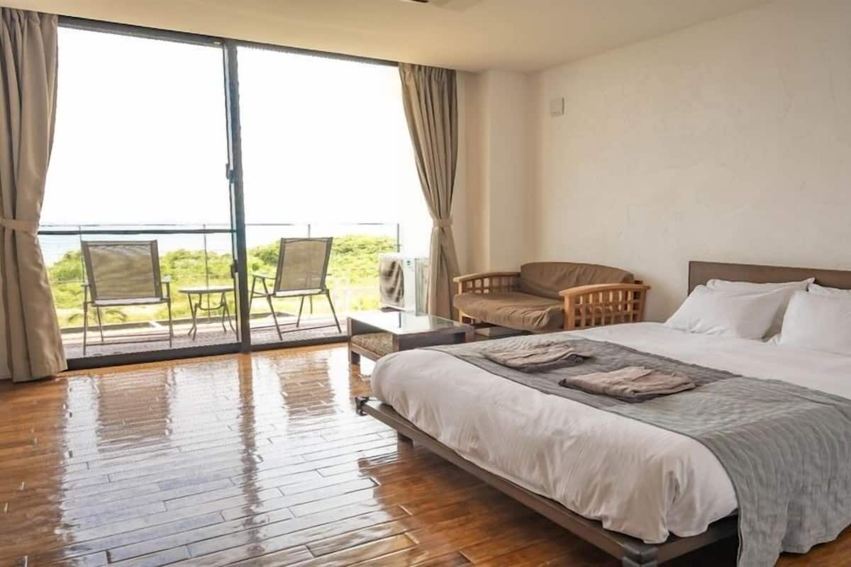 A bedroom with a large bed, a sofa, a chair, and a balcony with a view.