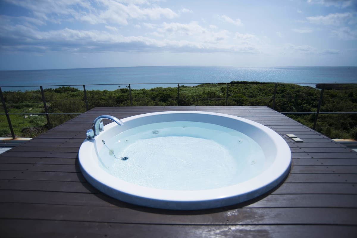 A hot tub on a wooden deck with a view of the ocean.