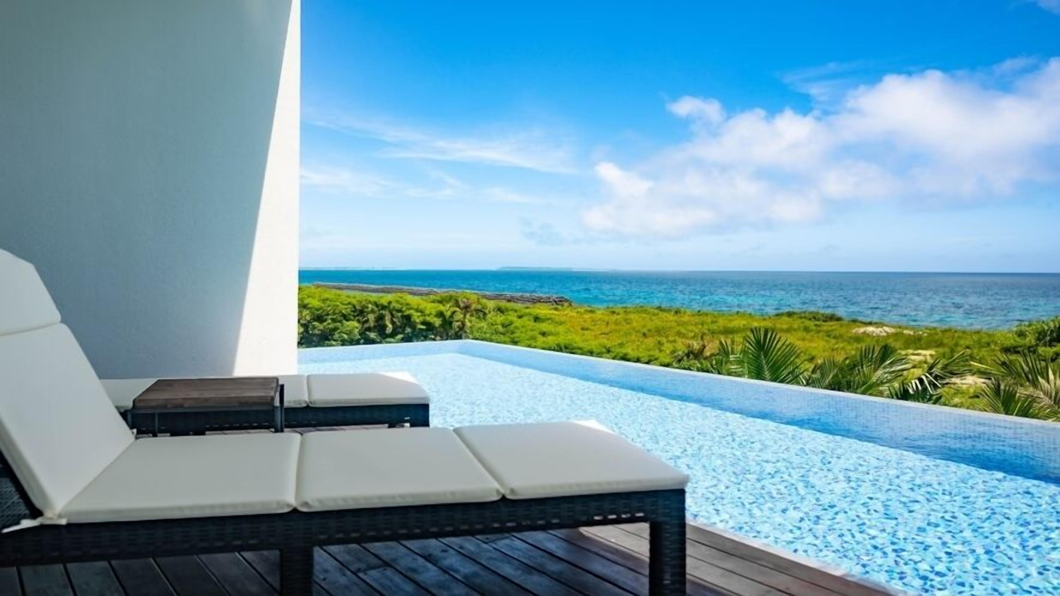 A lounge chair by a pool with a view of the ocean and greenery.