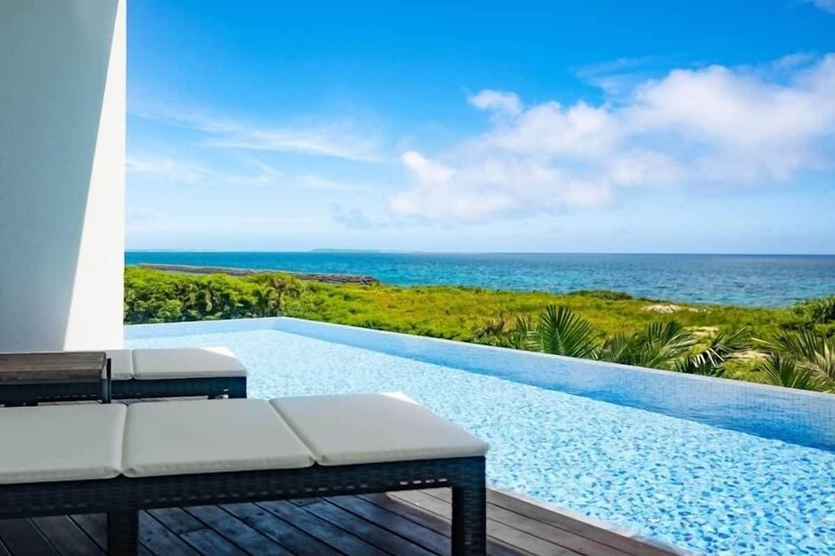 A lounge chair by a pool with a view of the ocean and greenery.