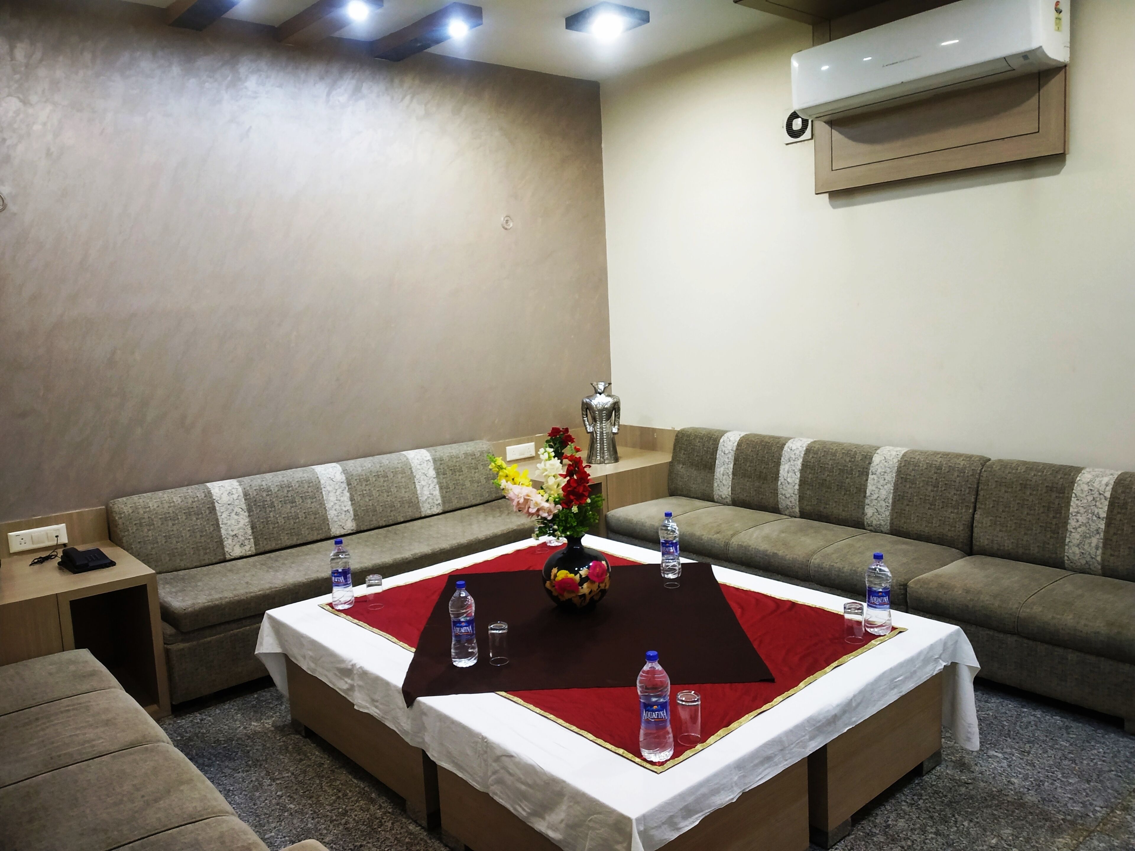 A modern hotel room with a sectional sofa, a small table with a red runner, and a decorative vase.