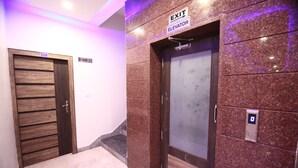 Un ascensor y una escalera en un pasillo con pared de mármol y puerta de madera.