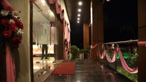 Entrada de hotel con alfombra roja, cortinas rosas y adornos florales.