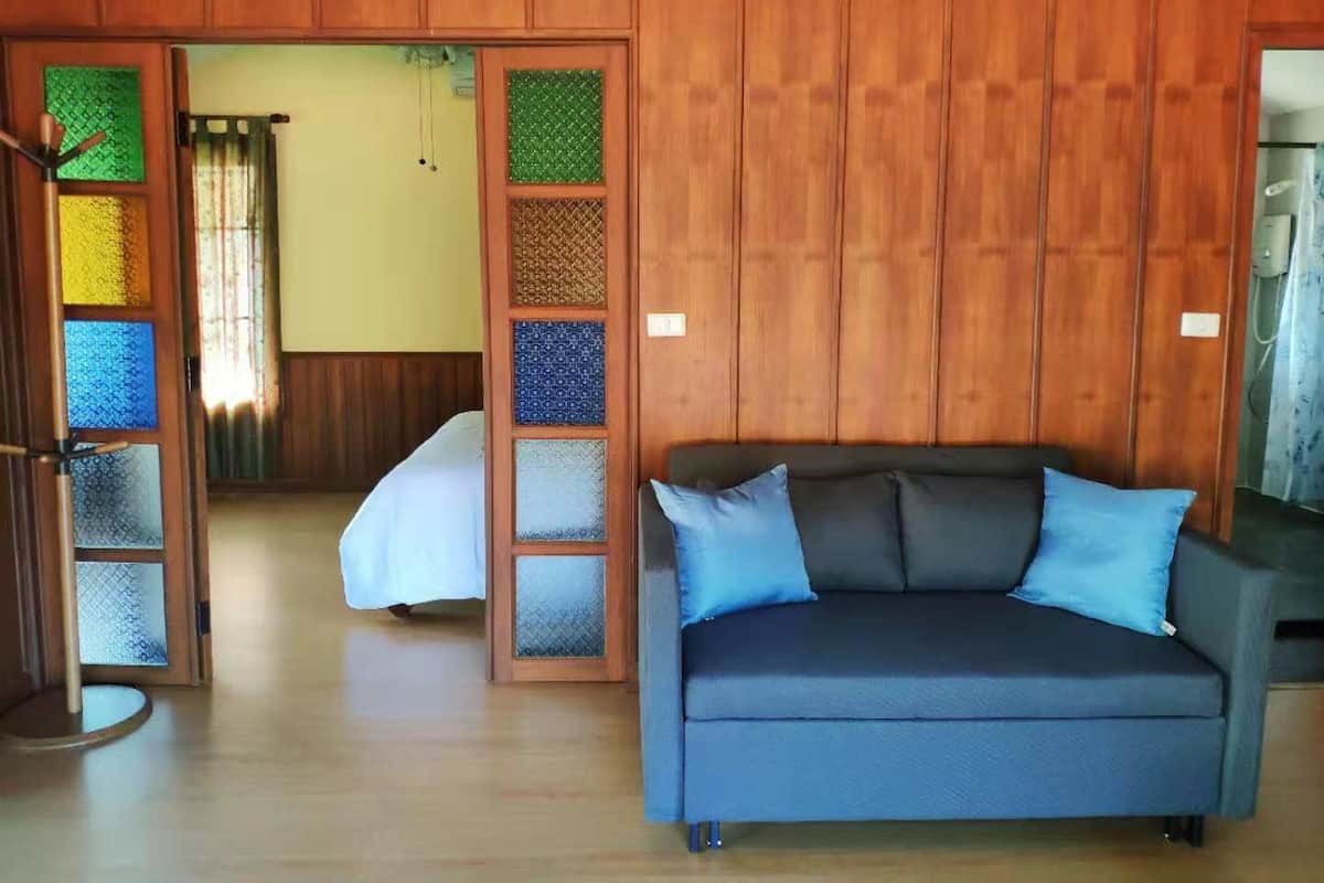 Une pièce avec un canapé bleu foncé, une porte en bois ornée de panneaux de verre colorés et un lit recouvert d’une couverture blanche.