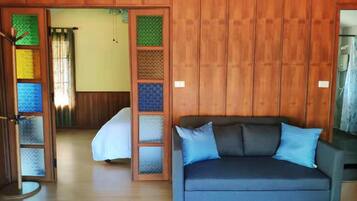 Una habitación con un sofá azul oscuro, una puerta de madera con paneles de vidrio de colores y una cama con una colcha blanca.