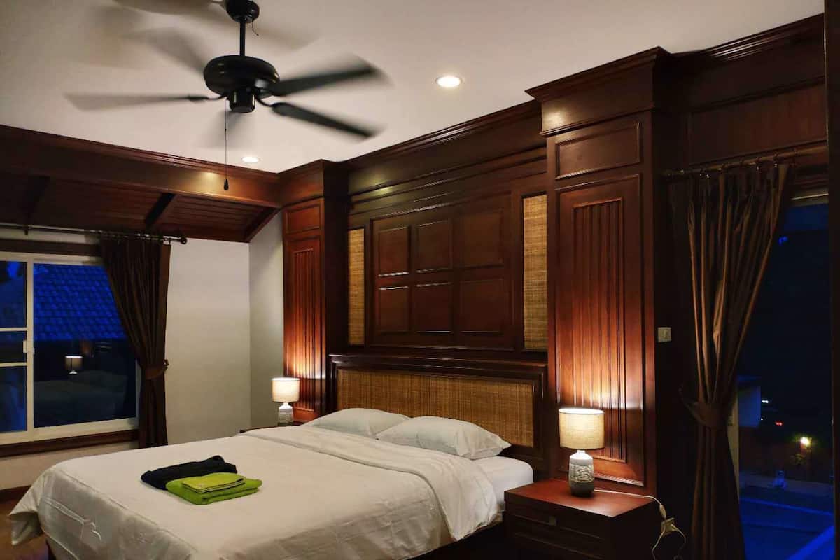 Une chambre d’hôtel avec un lit, deux tables de chevet, un ventilateur de plafond et une fenêtre avec des rideaux.