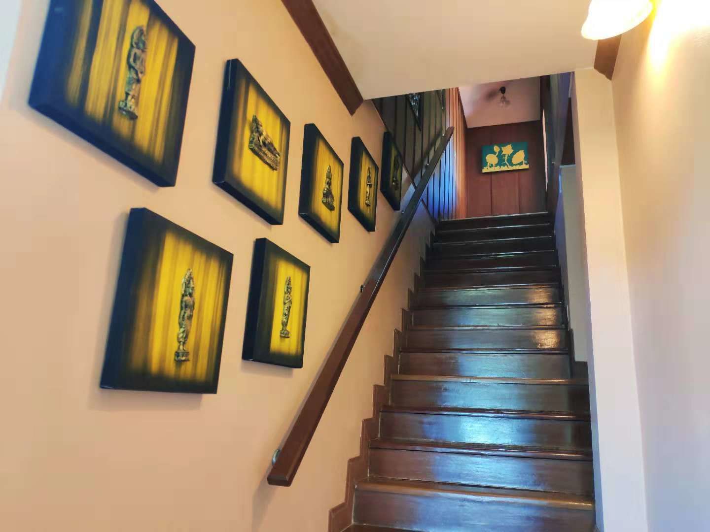 Una scala in legno con corrimano, che conduce a un pianerottolo con una porta in legno e un punto luce fissato al muro.