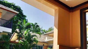 A balcony with wooden chairs and a table, overlooking a pool and lush greenery. - Momoka Luxury Villa (San Sai)