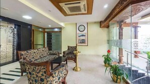 A lobby with a sofa set, a coffee table, a clock on the wall, and potted plants.