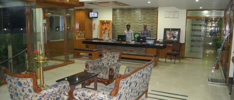 A hotel lobby with a reception desk, seating area, and a television screen.