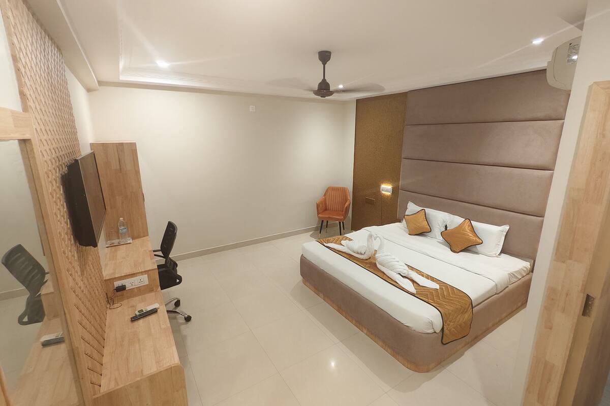 Une chambre d’hôtel moderne avec un grand lit, un bureau en bois, une chaise et un ventilateur de plafond.