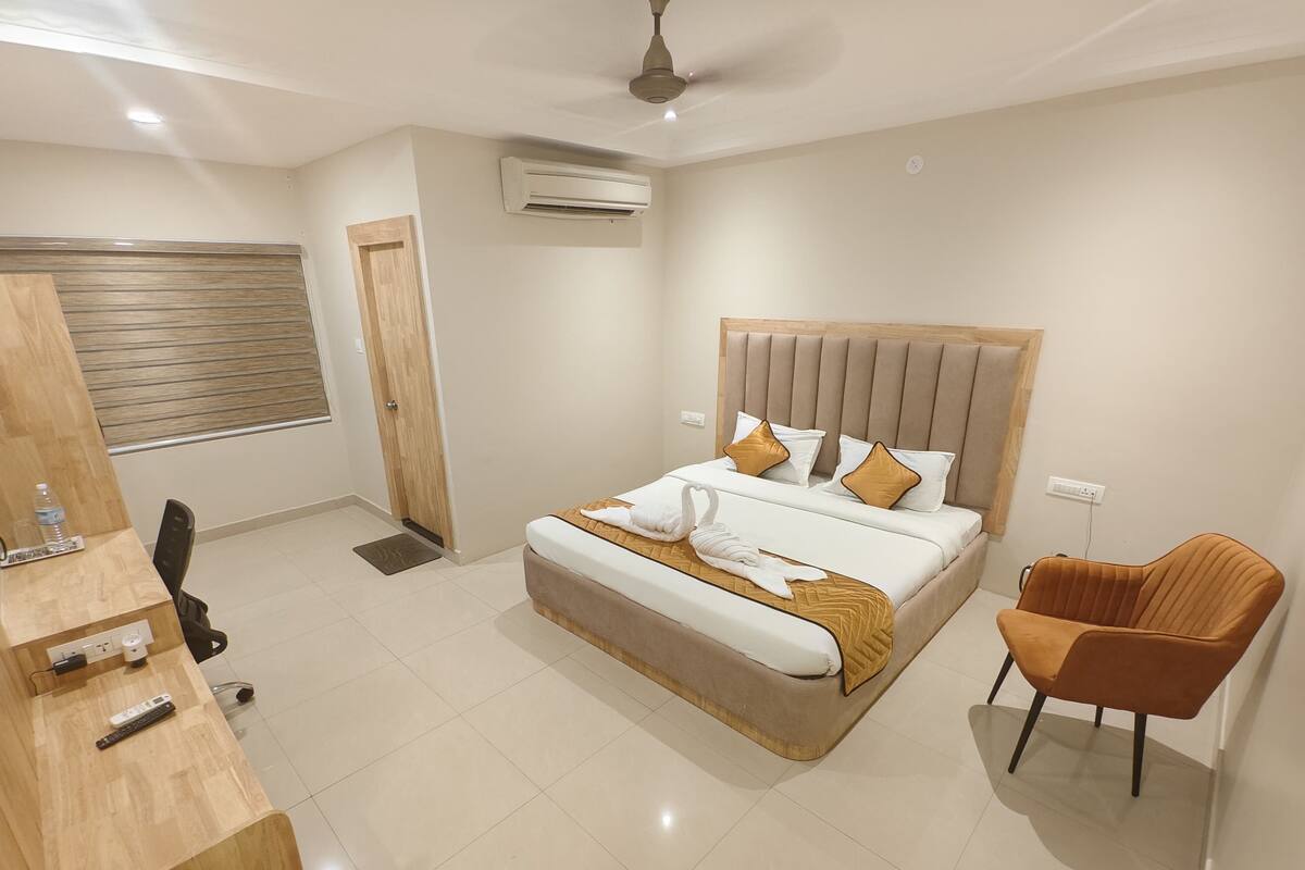 Une chambre d’hôtel moderne avec un grand lit, un bureau en bois, une chaise et un ventilateur de plafond.
