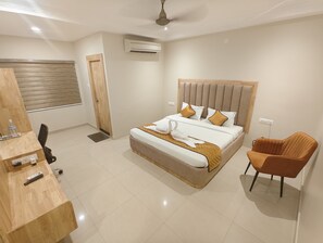 Een moderne hotelkamer met een groot bed, een houten bureau, een stoel en een plafondventilator.
