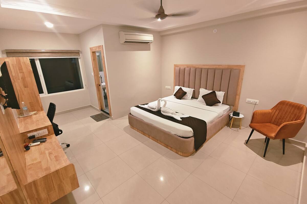 Une chambre moderne avec un grand lit, un bureau en bois, une chaise orange et un appareil de climatisation.